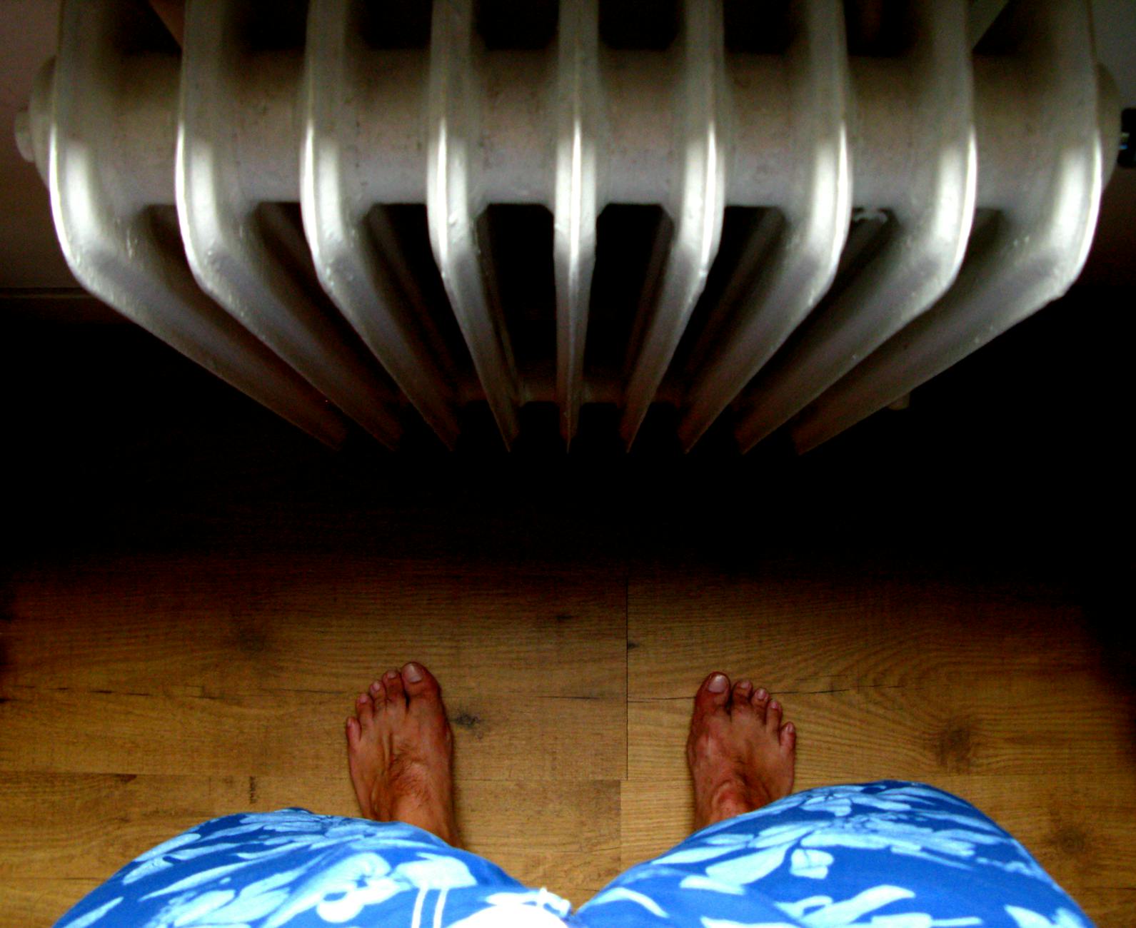 Stopy boso na drewnianej podłodze obok włączonego kaloryfera